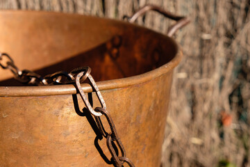 Copper chain and copper cauldron. Cooking outdoor. Sunlight. Hard shadows.