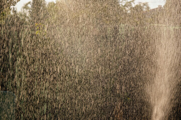Water jet spraying. Splashing water background in evening golden hour in Provence. 