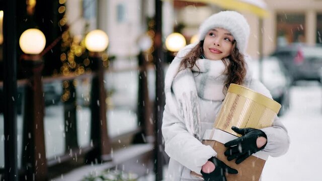 Close up portrait of female in snowy holiday city. Snowing outdoors. Magic moment young beautiful blonde woman walking outdoors with Gift box