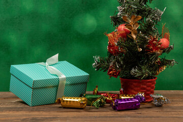 Green gift box with bow on blurred green background and Christmas tree ornament.