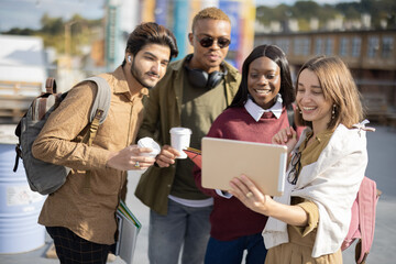 Multiracial students watching something on digital tablet outdoors. Concept of education and learning. Idea of students lifestyle. Young guys and girls at university campus. Black men with coffee