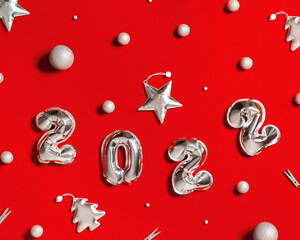 New Year 2022 silver balloons number and soft toys shape as Christmas tree and bright star, decorated balls on red cloth background. Winter celebration cards