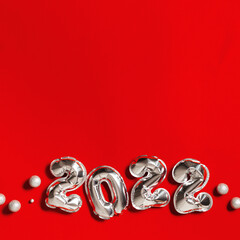 New Year 2022 silver balloons number decorating small balls on red fabric background with copy space. Greeting card or invitation for new year party
