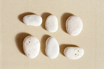 Sea stones neutral beige color on natural fine sand background. Square composition from natural white pebbles, monochrome tones