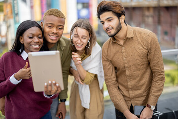 Multiracial students watching something on digital tablet outdoors. Concept of education. Remote and e-learning. Idea of student lifestyle. Smiling young friends at university campus