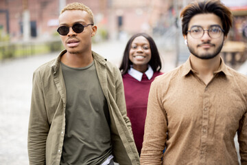 Multiracial students walking on territory of university campus. Concept of education and learning. Idea of student lifestyle. Young serious guys and smiling girl in casual clothes