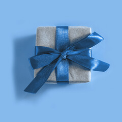 The above view on the present packed in the craft paper with the blue satin ribbon on the blue background. Minimalism New Year or Christmas concept.