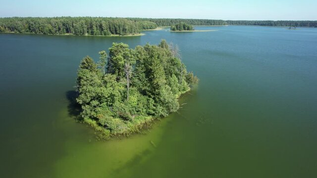 Slow drone flight low over the lake and small green island. Aerial view in a sunny day.