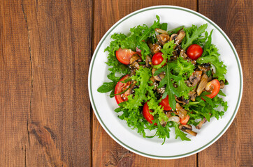 Diet salad of arugula leaves, tomatoes and fried mushrooms on wooden table. Studio Photo