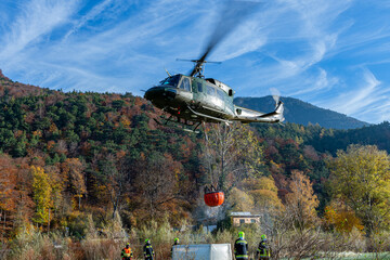 An Austrian Armed Foreces Helicopter immeres a water Bucket to fight a forest fire from the Air