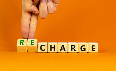 Charge or recharge symbol. Businessman turns wooden cubes and changes the word 'charge' to 'recharge'. Beautiful orange table, orange background. Business charge or recharge concept. Copy space.
