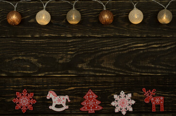 Dark brown wooden background with a garland on top and decorative Christmas figures made of wood on the bottom. Brown, red and white colors. Selective focus.
