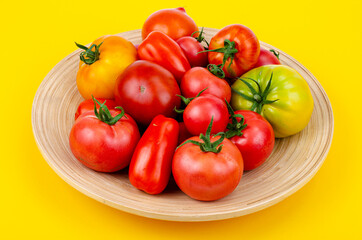 Mix of ripe colorful tomatoes on bright yellow background. Studio Photo