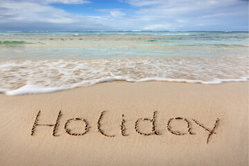 Word Holiday written on the sand near the sea.