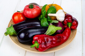 Plate with bright ripe vegetables on white wooden table. Studio Photo.