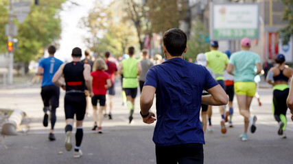 Man wearing blue t-shirt and earphones running on empty city road, blurred crowd of athletes...