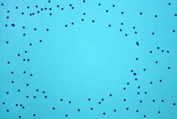 Blue festive background with scattered bright shiny star confetti. Empty space. Birthday, party, Christmas, New Year.