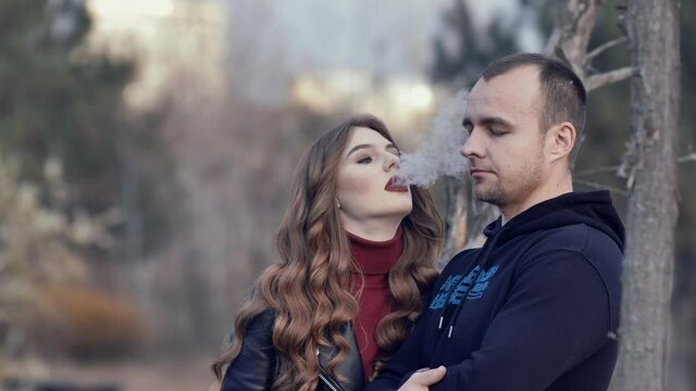 beautiful girl smokes an electronic cigarette blowing smoke at her boyfriend. a pair of millennial