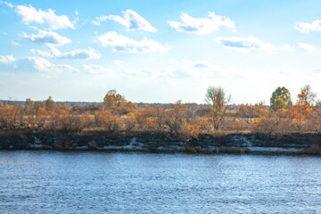 Beautiful clouds in the blue sky. Autumn landscape on a bright sunny day. Yellow trees and bushes on the opposite bank of the river.
