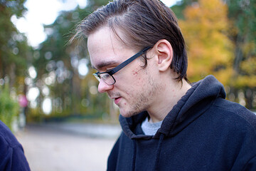 Naklejka na ściany i meble A young guy in a black hoodie with glasses looks down.