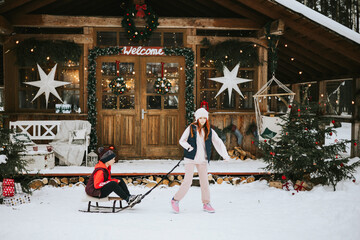 two children boy and teenage girl on porch of village house having fun and sledding each other...
