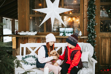 two children boy and teenage girl with poodle dog sitting on porch of village house and having fun during Christmas winter holidays, Christmas and New year vacation concept