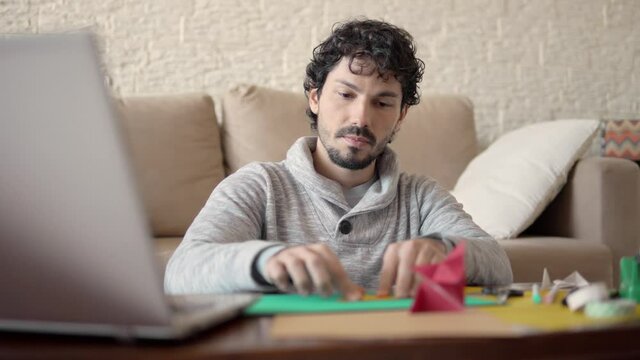 young adult folding paper for origami. leisure and learning new skill online, with laptop