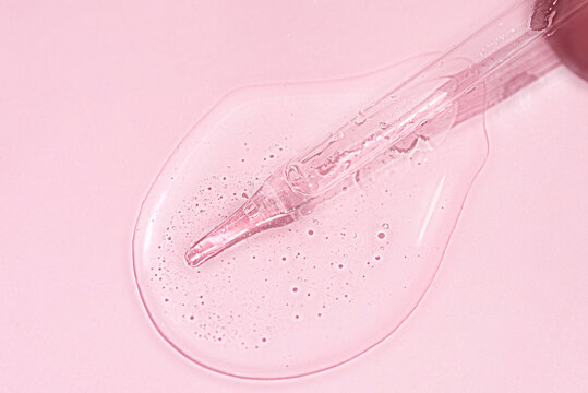 Liquid oil serum drop in pipette isolated on pastel pink background. Retinol, aha acid, collagen skincare fluid, photo with shallow depth of field. Hyaluron essence in dropper for beauty treatment