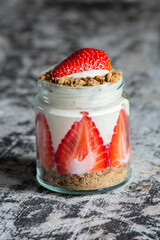 insulated glass jar with yoghurt, strawberries and biscuits on a wooden board. delicious dessert
