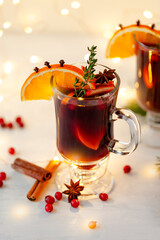 A glass with hot winter drink: 
red mulled wine with spices, fruits. Christmas lights on background. Cozy atmosphere.