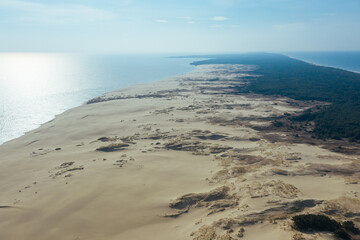 A view from a height of a narrow and long sandy saber-shaped strip of land separating the Curonian Lagoon from the Baltic Sea. Gray sand dunes of the Curonian Spit.