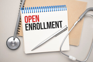 White notepad with the words open enrollment and a stethoscope on a blue background. Medical concept
