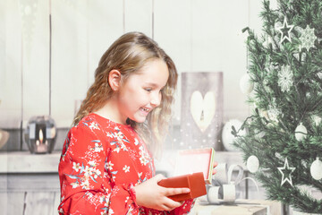 Little girl at home in red dress opening gift box at christmas