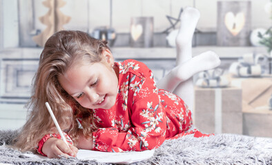 Girl lying at home in red dress writing letter for christmas