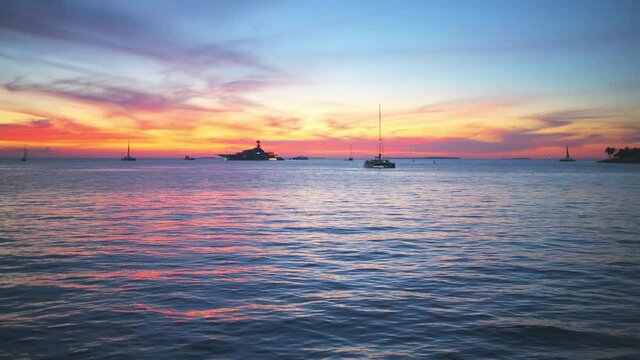Silhouettes of boats, yachts at colorful sunset twilight blue hour dusk with landscape view on blue cloudy clouds sky by Mallory Square of Key West, Florida