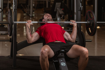 Fit young man lifting barbells working out in a gym