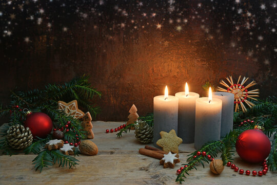 Third Advent, three of four candles are lighted, red baubles, branches and gingerbread cookies as Christmas decoration on rustic wooden planks, dark brown background with copy space