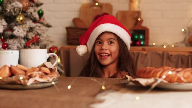 little girl in a Santa hat and a dwarf dachshund want to eat a plate of pastries and a Christmas cake standing on the table in the kitchen decorated for the new year. High quality 4k footage