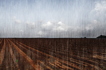 Rain on a plowed field. The photo effect of raindrops and torrential rain through a window pane