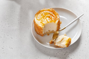 cheesecake with yellow top with spoon on a saucer on a gray background