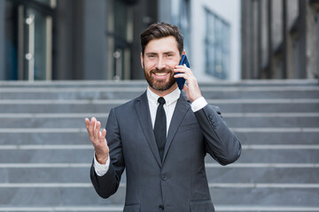 portrait successful young confident businessman talking background urban modern office building in downtown Bearded business man conversation a mobile phone standing in formal suit outdoor city street