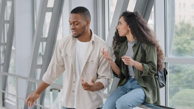 Multiracial couple hispanic woman and african man travelers sitting at airport in new country looking for route direction road shouting arguing conflict guy throws map disappointed offended walks away
