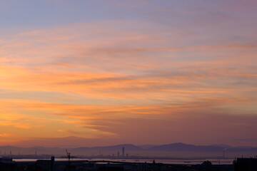 Fototapeta na wymiar 都市の夜明け。日の出とともに空と雲がオレンジ色に染まる。遠くに大阪湾を臨む