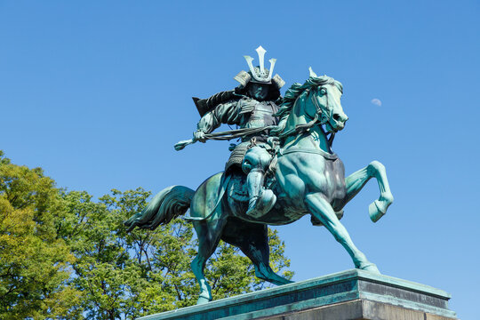 皇居前の馬に乗った楠木正成の銅像、青空と昼間の月と緑のの背景