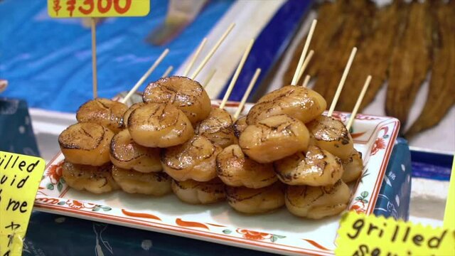 Eating hotate sashimi. Merchants sale deliceous scallop in Nishiki fish market. Fish and seafood retail shops in Japan. A japanese sushi take out stalled-Dan