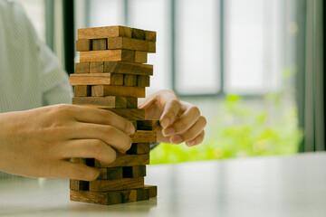 Hand pulls wooden blocks out of towers, growth, risk, and business strategy. close-up photo of woman's hand