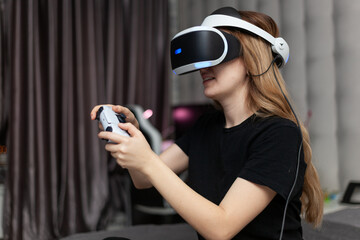 young woman in virtual reality helmet with gamepad joystick playing