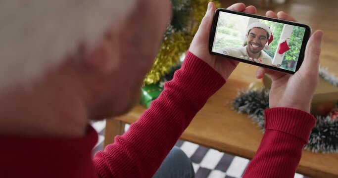 Caucasian man with santa hat using smartphone for christmas video call with smiling man on screen