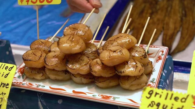 Slow motion of eating hotate sashimi. Merchants sale deliceous scallop in Nishiki fish market. Famous asian raw seafood meal. Traditional menu food and healthy eating-Dan