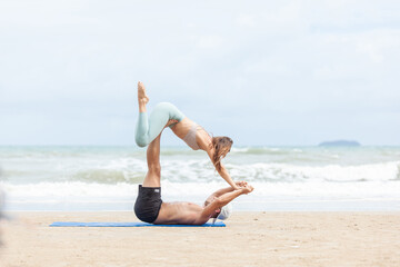 Fototapeta na wymiar fitness, sport, and lifestyle concept - couple making yoga exercises on beach, Man and woman doing yoga exercise on the beach.